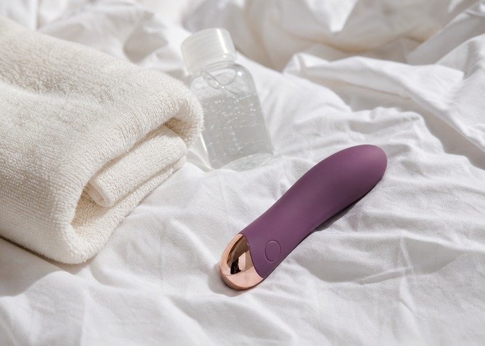 A realistic cleaned personal wellness device with a towel and pouch arranged for an adults-only aftercare and storage guide.