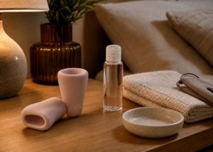A realistic male-toy comparison setup with an automatic masturbator, a manual sleeve, lubricant, towel, and storage pouch on a bedside table.