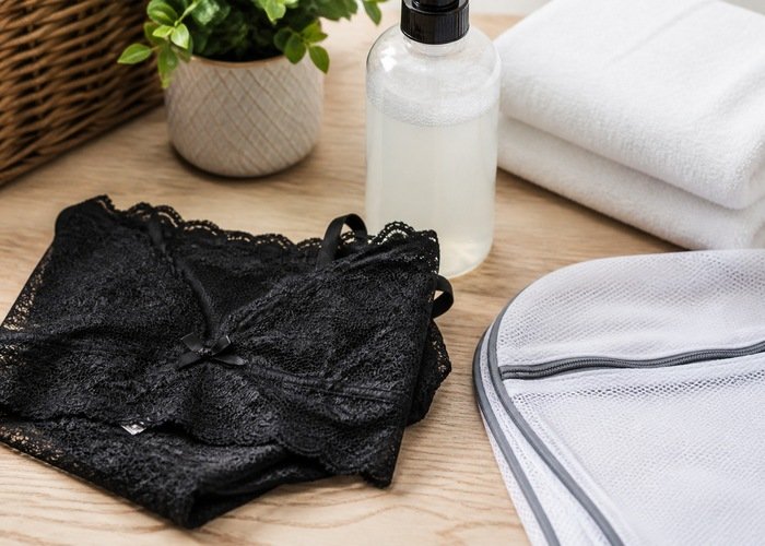 A lace bralette and mesh lingerie in a wash bag beside a basin and towel.