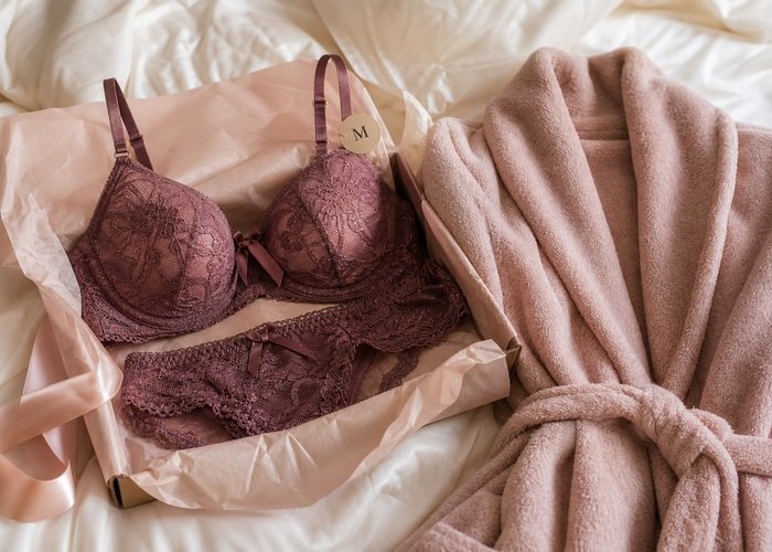 A wrapped lingerie gift box with adjustable straps, size tag, and soft robe arranged for a considerate lingerie present.