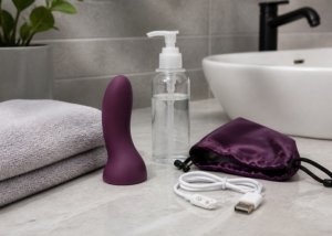 A curved personal wellness device with a stable base, towel, pouch, and cable on a bathroom vanity.