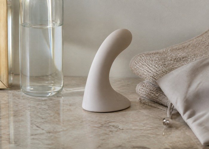 A close countertop setup with a curved prostate massager, lubricant, towel, and pouch arranged to explain angle and base fit.