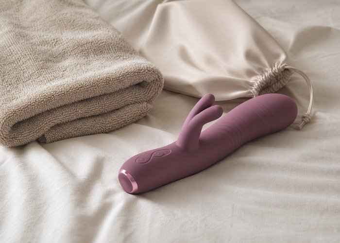 A realistic rabbit vibrator, compact suction toy, wand-style toy, and folded towel arranged on a bed for a comparison guide.