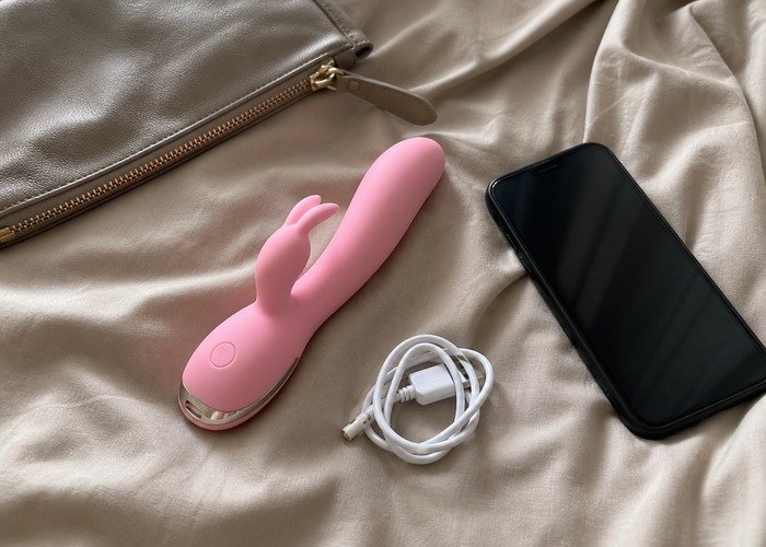 A realistic bedside setup with a phone, compact vibrator, charger, and pouch arranged for a remote versus app-controlled vibrator guide.