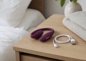 A realistic vibrator, charging cable, and soft pouch arranged on a bedside table for a storage guide.